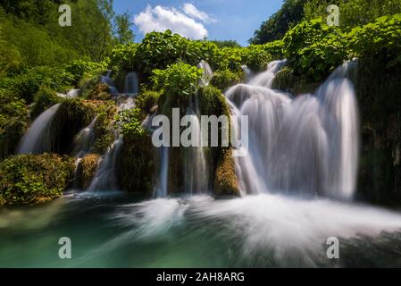 Iconica vista ad angolo basso di una cascata croata circondata da vegetazione sotto un cielo blu con nuvole puffy Foto Stock