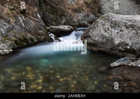 Primo piano di un torrente di montagna che scorre tra rocce bianche e scende rapidamente in un laghetto cristallino Foto Stock