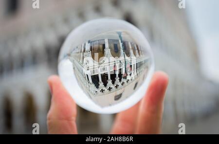 Primo piano di una mano che tiene una palla di cristallo che riflette il Palazzo del Duca di Venezia, su uno sfondo bokeh Foto Stock