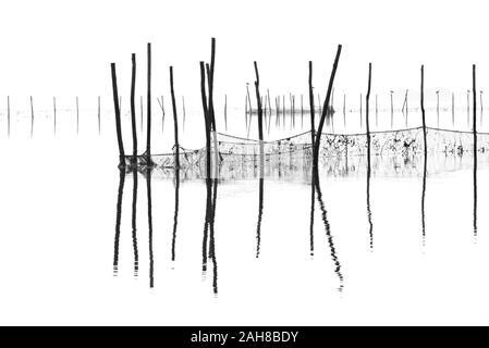 Caratteristico paesaggio foggy veneziano bianco e nero, con reti da pesce e pali che emergono dall'acqua Foto Stock