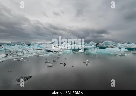 Ampia vista della laguna islandese dell'iceberg, con un certo numero di iceberg che galleggiano in primo piano e un ghiacciaio distante sullo sfondo Foto Stock