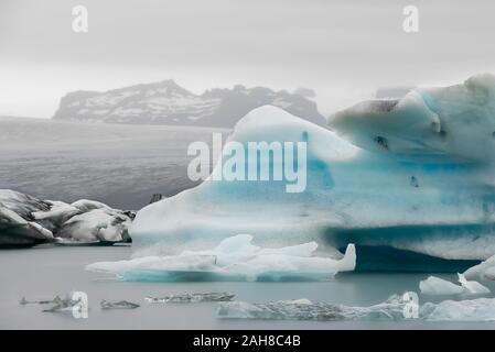 L'iconico paesaggio islandese con un iceberg galleggiante in primo piano e un ghiacciaio lontano sullo sfondo Foto Stock