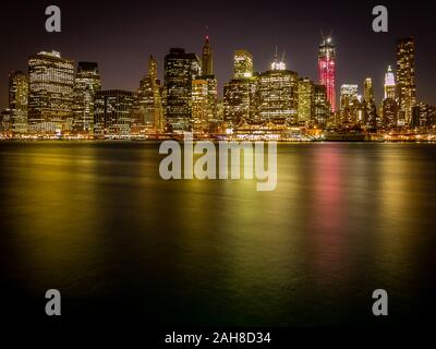 Grandangolo notturno dello skyline di Manhattan visto dalla Brooklyn Heights Promenade, con luci della città che si riflettono sull'acqua Foto Stock