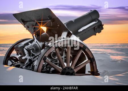 Primo piano di un cannone della prima guerra mondiale su un monumento coperto di neve in cima alla montagna all'alba Foto Stock