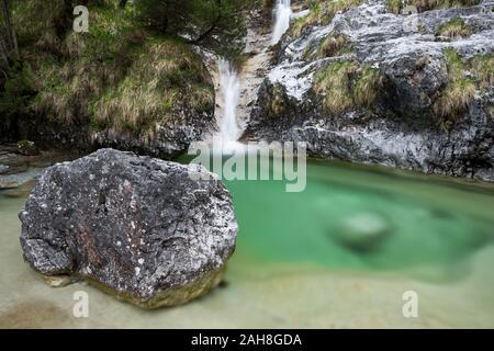 Ampio angolo di vista di un torrente di montagna che scorre tra rocce bianche e in uno stagno verde smeraldo, con un masso in primo piano Foto Stock