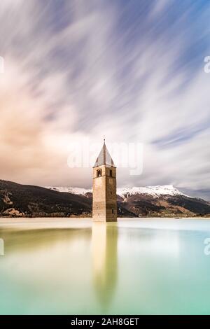 Ampia visuale simmetrica di un vecchio campanile allagato in un lago artificiale nel nord Italia Foto Stock