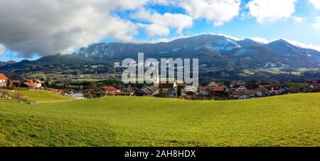 Vista sulle montagne delle Alpi, cielo blu e nuvole, campo verde, chiesa di Samerberg, Hochries, Baviera, Baviera, Germania Foto Stock