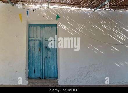 Blu porta in legno e tetto di paglia con drammatica i raggi di luce e le ombre a abadoned chiesa Ermita de Sant Antoni y Sant Jaume nel cappuccio Blanche, Altea, Spai Foto Stock