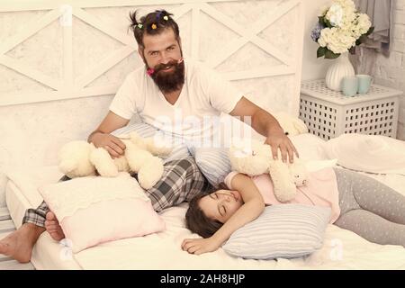 La fine della serata pazzo. Avendo divertimento pigiama party. Slumber party. Felice della paternità. Papà e una ragazza rilassante camera da letto. Pigiami stile. Padre uomo barbuto divertente ponytails di acconciatura e la figlia in pigiama. Foto Stock