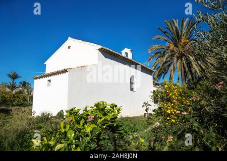 Chiesa Abadoned Ermita de Sant Antoni y Sant Jaume tra palme e piante verdi con cielo blu senza nuvole nel cappuccio Blanche , Altea, Spagna Foto Stock