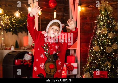 Ciao santa. Little Boy in rosso le renne maglione. kid a santa claus hat divertirsi a casa. Buon Natale a tutti. Vuole xmas presente. le migliori vacanze invernali. Felice adolescente di celebrare la festa di capodanno. Foto Stock