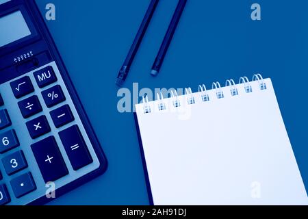 Blocco note con due matite e una calcolatrice su uno sfondo giallo, tonica trendy classico colore blu dell'anno 2020 Foto Stock