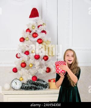 Bambino festeggiano il Natale a casa. Giorno preferito dell'anno. Il tempo di aprire i regali di Natale. Aprire i Regali di natale. Sogni. Il meglio per i nostri bambini. Kid ragazza nei pressi di albero di natale in attesa di confezione regalo. Foto Stock