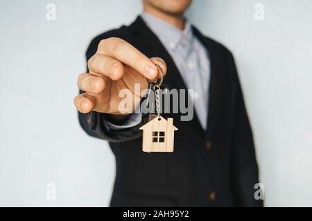 Tenendo fuori le chiavi di casa su una casa portachiavi sagomato. concetto di vendita di un bene immobiliare. Affittando un appartamento. Affittare una camera. Foto Stock