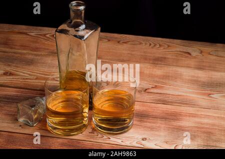 Due bicchieri di whiskey stand accanto al decanter su un tavolo di legno. Occhiali con il whiskey senza ghiaccio. Foto Stock