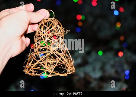 Foto frontale di una campana artigianali realizzate in vimini, trattenuto da una mano di un giovane uomo caucasico con un background di unfocused luci colorate e uno spazio libero Foto Stock