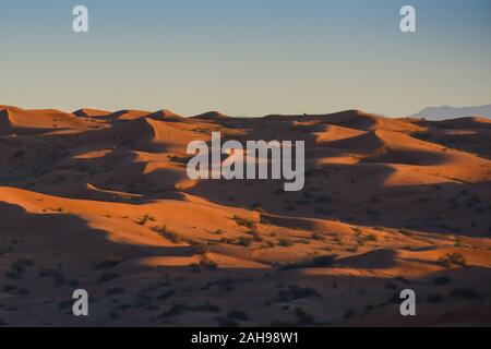 Deserto di sunrise mette in evidenza in grassetto arancione bruciato sabbia colorata con ombre che rendono un grande paesaggio del deserto su ondeggiano o le colline di Ras al Khaima Foto Stock