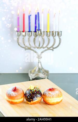 Hanukkah celebrazione del concetto. Vista ravvicinata di gustose ciambelle con marmellata e cioccolato sullo sfondo il menorah candelabri tradizionali con illuminazione candele. Foto Stock