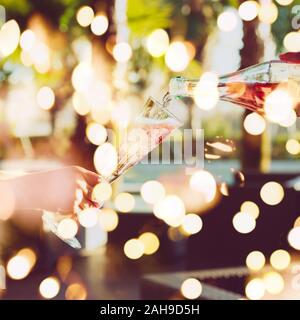Cameriere è pourring vino spumante in una donna di vetro al party all'aperto. Celebrazione del concetto. Evento, party, matrimoni sfondo. Tonica immagine. Quadrato con festosa luci bokeh di fondo Foto Stock