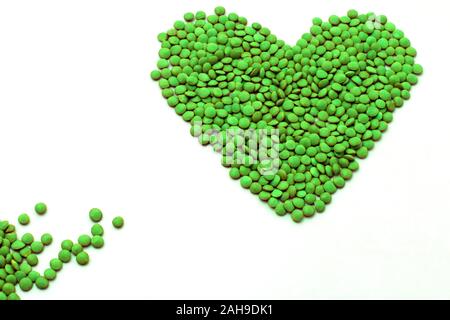 Una forma di cuore fatta di lenticchie colorate in verde brillante, isolato su uno sfondo bianco Foto Stock