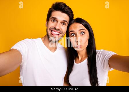 Foto di due persone in stato d'animo stolto tenendo selfies aletta di incollaggio, rendendo volti indossare abiti casual isolato giallo colore di sfondo Foto Stock