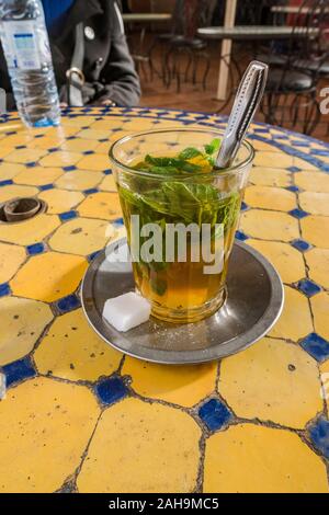 Vetro tradizionale con tè alla menta su un tavolo piastrellato. La medina di Marrakech, Marocco Foto Stock