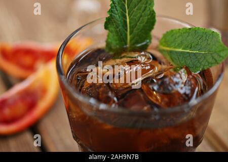 Cocktail whiskey cola con ghiaccio in un bicchiere. Su una tavola di legno sono frammenti di frutta. Foto con profondità di campo. Foto Stock