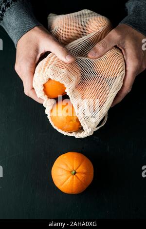 Primo piano di un uomo con un tessile riutilizzabile borsa a rete, utilizzato per acquistare generi alimentari alla rinfusa, pieno di arance, come misura per ridurre l'inquinamento in plastica Foto Stock