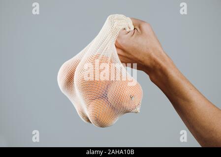 Primo piano di un uomo con un tessile riutilizzabile borsa a rete, utilizzato per acquistare generi alimentari alla rinfusa, pieno di arance, come misura per ridurre l'inquinamento in plastica Foto Stock