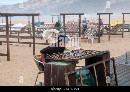 Pescivendolo vende sole asciugato di pesce sulla spiaggia a Nazare, Portogallo Foto Stock