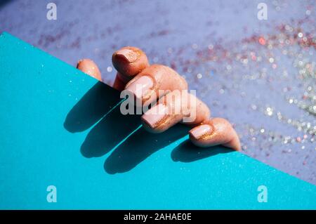 Giovane donna di mano con belle manicure minimalista e un sacco di decorazione di glitter su sfondo puple tenendo il colore blu della carta. Concetto di festa. Foto Stock