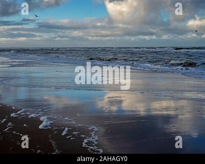 Drammatico il cielo blu con nuvole bianche si riflette sulla spiaggia bagnata con la bassa marea a Noordwijk nei Paesi Bassi Foto Stock