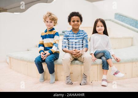 Piccolo gruppo interculturale di adorabili bambini seduti nella parte anteriore della fotocamera Foto Stock