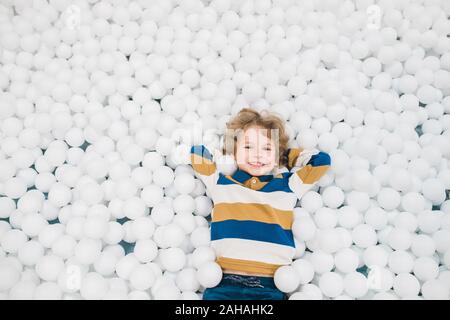 Adorabili e gioiosa ragazzino che giace tra i palloncini bianchi e divertirsi Foto Stock