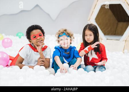 Gruppo di adorabili poco amici interculturale in costume in seduta palloncini Foto Stock