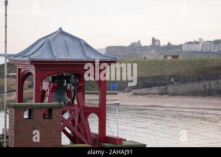 Una vista della stazione di RNLI torre campanaria a Cullercoats Harbour con il Priorato di Tynemouth in background Foto Stock