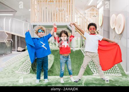 Due piccolo grazioso ragazzi interculturale in costumi di supereroi e ragazza asiatica Foto Stock