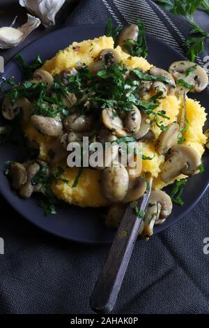 Concetto di cucina italiana. Vista superiore della polenta cremosa con sauté di funghi e prezzemolo fresco. Foto Stock