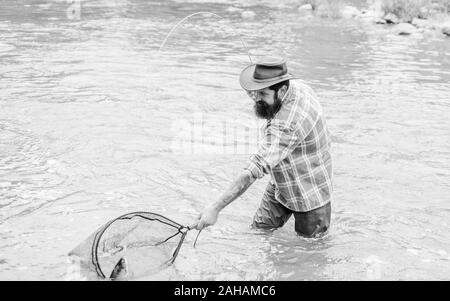 La pesca è un sorprendente accessibile ricreativo sport all'aperto. Barbuto brutale fisher la cattura di pesci trote con net. Se regolarmente del pesce si sa come gratificante e rilassante è la pesca. La pesca hobby. Foto Stock