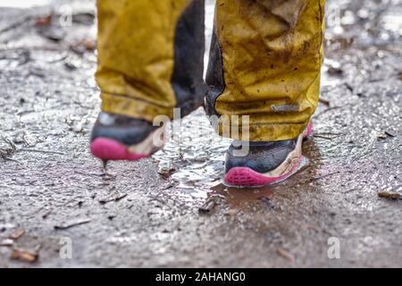 Norimberga, Germania - 25 dicembre 2019: sezione bassa di un bambino ragazza salti intorno con i suoi piedi su terreni fangosi e terra bagnata in una piovosa giornata d'inverno. Foto Stock