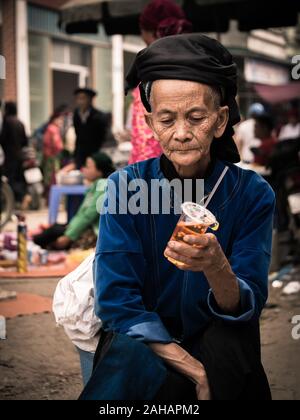 Anziana signora vietnamita di minoranza etnica in abiti tradizionali con una tazza di plastica di Dong Van mercato, Vietnam Foto Stock