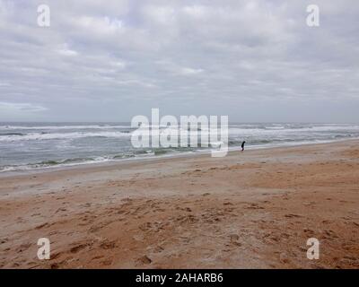 Giovane in felpa con cappuccio altrimenti sulla spiaggia vuota su un blustery giorno di dicembre con cappucci bianchi e le onde, Saint Augustine Beach, Florida, Stati Uniti d'America. Foto Stock