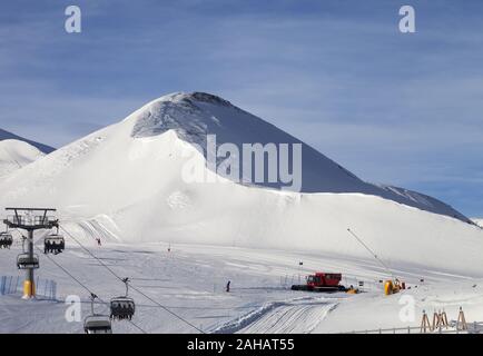 Snowy ski via preparate con neve macchina grooming, seggiovia, cannoni da neve e il gatto delle nevi in ski resort. Montagne nella soleggiata giornata invernale. Alpi italiane. Foto Stock