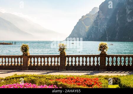 Lago di Garda promenade con aiuole fiorite con la crescita e la fioritura delle piante, classic recinzione in pietra costruito sul bordo con vasi da fiori con rigogliosi fl Foto Stock