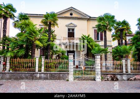 Abbandonato due piani classica casa italiana con crescente palm nel giardino recinto metallico e la porta d'ingresso a Riva del Garda, Lombardia, Italia Foto Stock