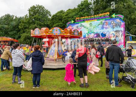 Orologi genitore di bambini su un dondoli ride in un paese giusto dopo il Thelwall Rose Regina processione 2019 Foto Stock