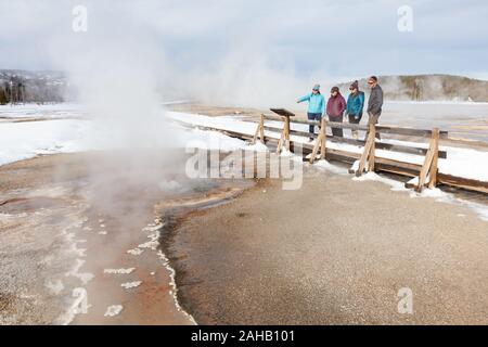 Un gruppo di turisti guarda la cannella Spouter geyser dal lungomare in Upper Geyser Basin durante l inverno al Parco Nazionale di Yellowstone a Yellowstone, Wyoming. Il parco è a casa per la metà dei mondi numero totale di geyser, contenente migliaia di sorgenti calde e circa 300 a 500 geyser. Foto Stock