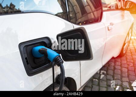 Close up di alimentazione inserito in una macchina elettrica essendo caricato mentre parcheggiate lungo una strada di ciottoli in un centro della città su awinter giorno Foto Stock