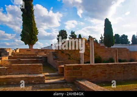 Brown di pareti in mattoni, colonne bianche e verdi cipressi antica città romana Italica, Siviglia, Spagna. Cielo blu e nuvole bianche come sfondo Foto Stock