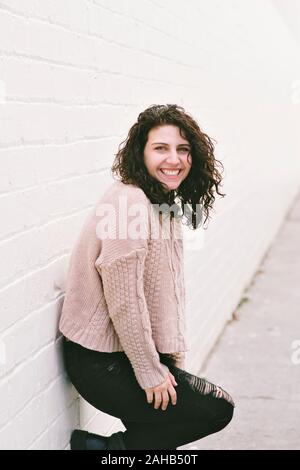 Giovane femmina la millenaria si appoggia contro una parete con un grande sorriso e allegro swashbuckling - ore diurne Foto Stock